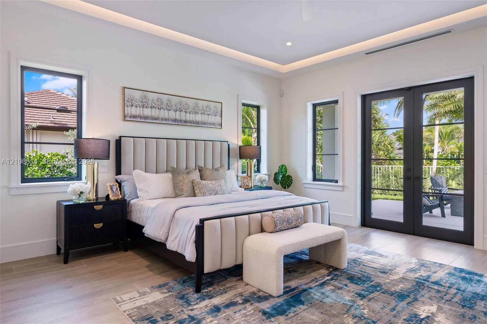 Tray ceiling with integrated recessed lighting, light-toned porcelain-finish flooring, and black-framed windows and dual-lite French doors