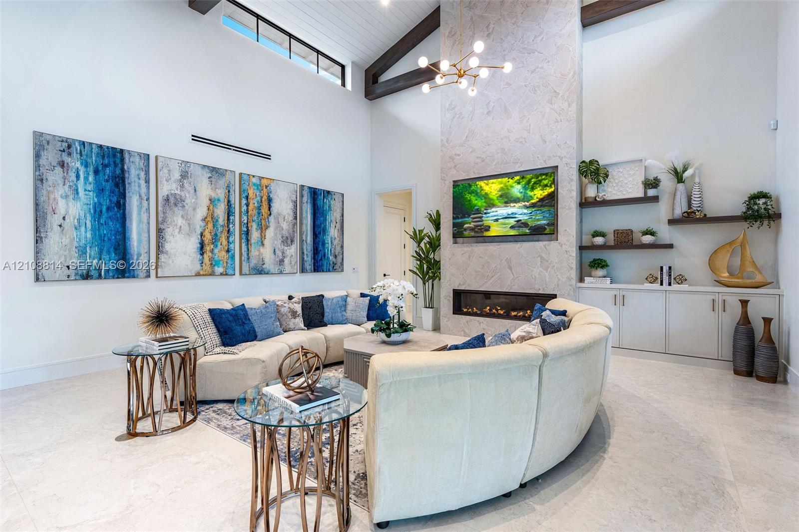 Vaulted ceiling with exposed wood beams, floor-to-ceiling stone-surround fireplace, linear electric firebox, clerestory windows, and built-in lower cabinetry with floating wall shelves