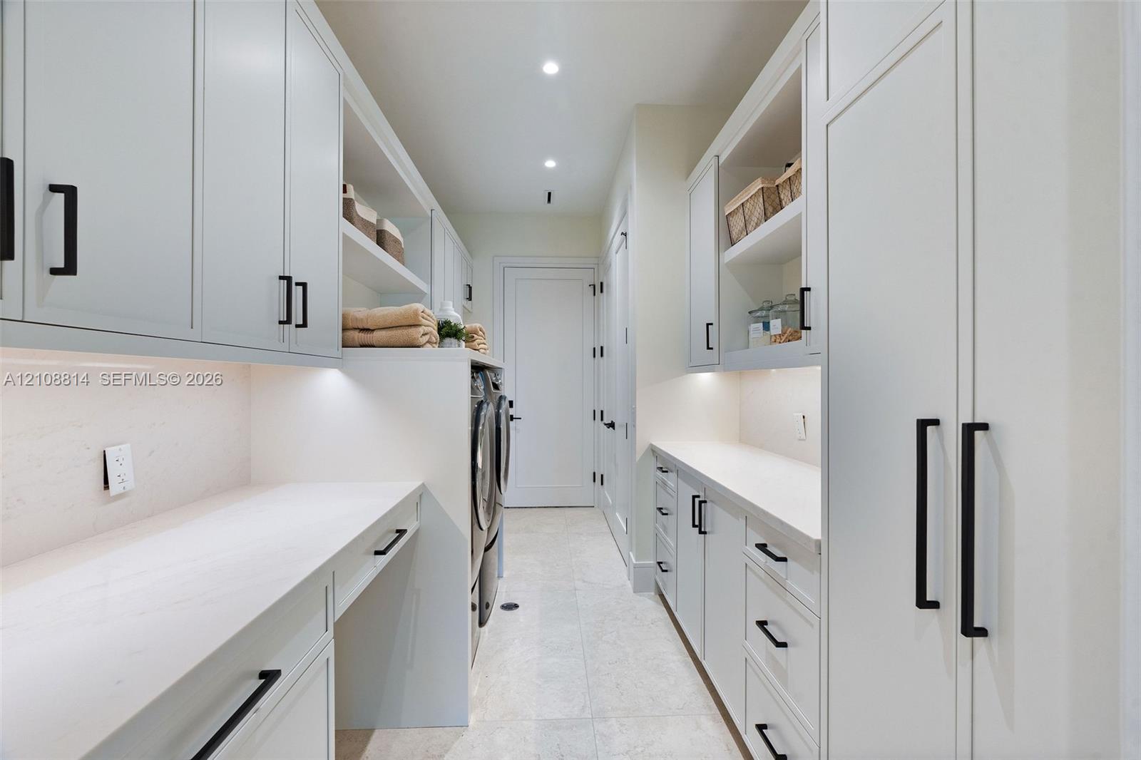 Custom cabinetry with matte black hardware, stone countertops, integrated under-cabinet lighting, and light-toned tile flooring