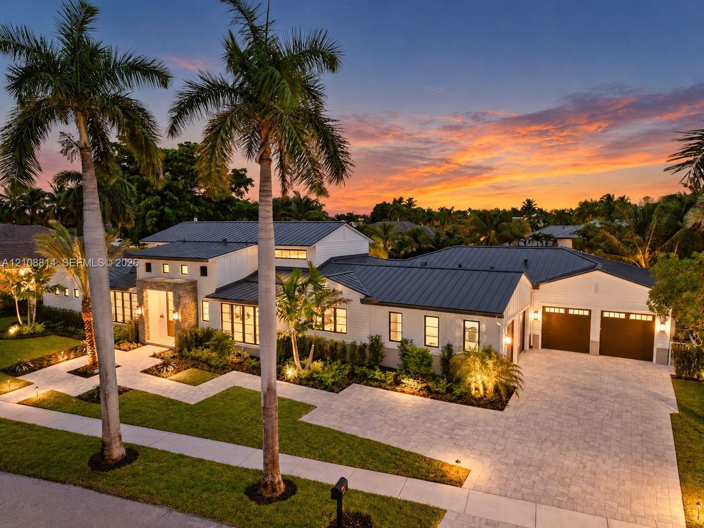 Modern architectural exterior featuring a metal roof, stone facade accents, multi-pane windows, and a paved driveway leading to an attached two-car garage