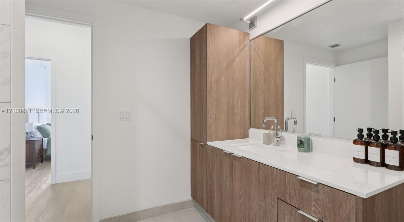 Built-in floor-to-ceiling cabinetry, vanity with quartz countertop, undermount sink, chrome faucet, and large-scale vanity mirror