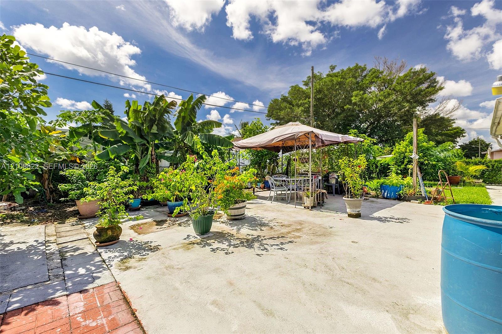 Concrete patio featuring decorative red brick edging, mature perimeter landscaping, and established greenery