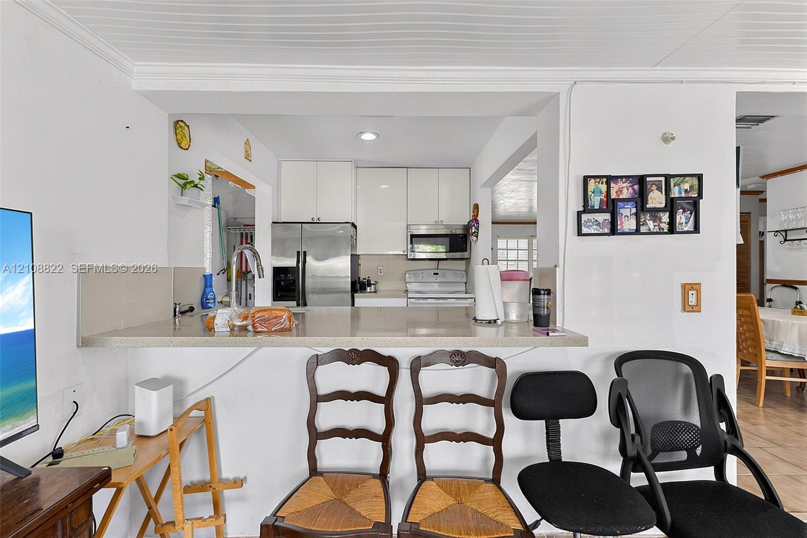 Kitchen featuring white cabinetry, a flat-surface countertop with an integrated bar, a stainless steel refrigerator, and a built-in microwave