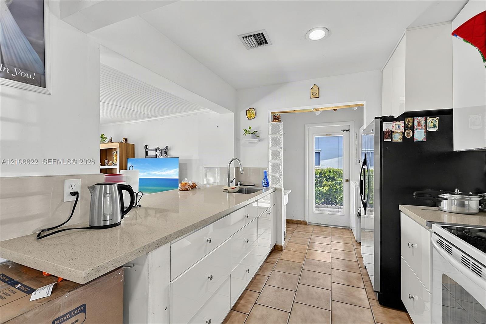 Kitchen featuring white flat-panel cabinetry, quartz countertops, tile flooring, and a glass-block framed door