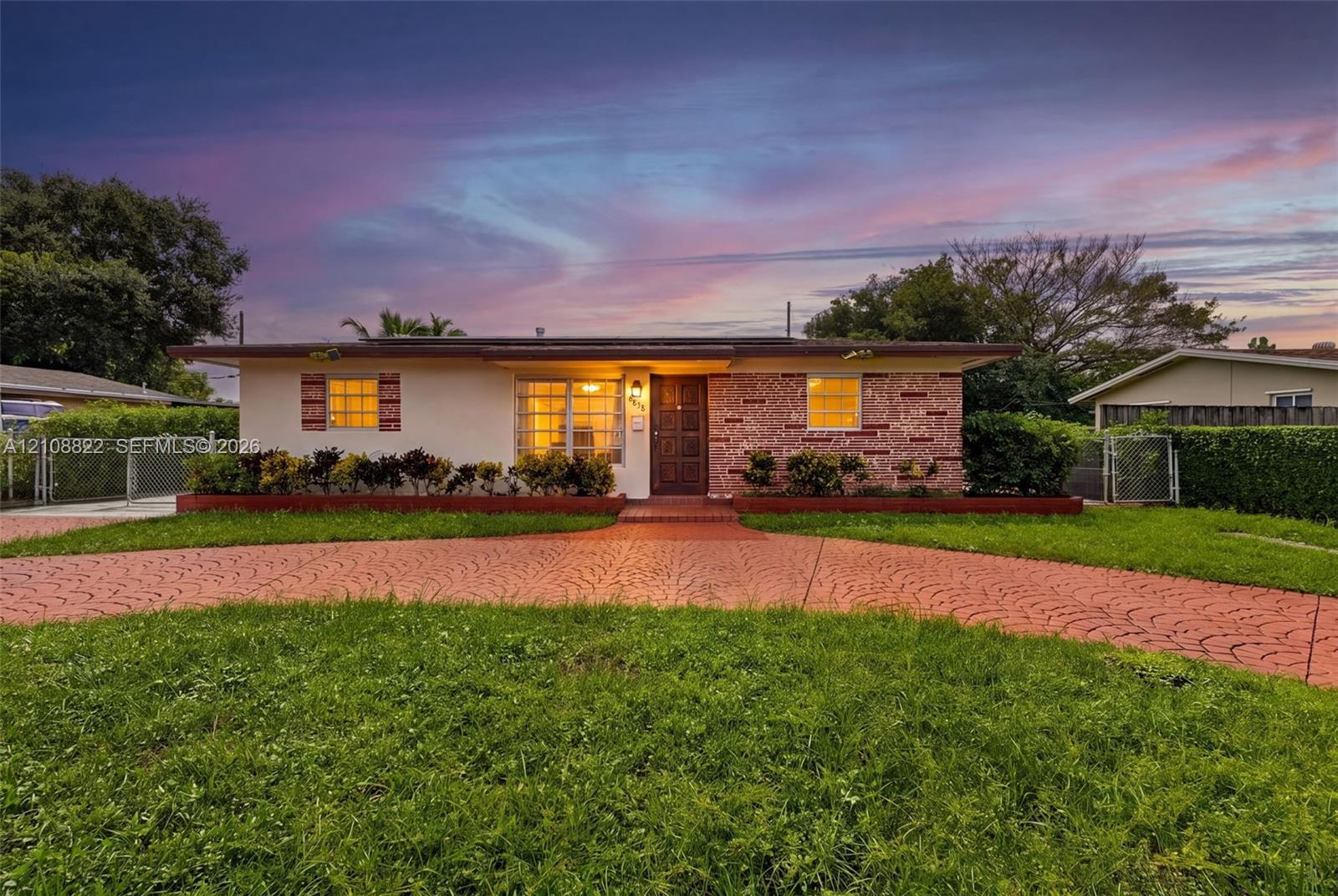 Single-story exterior featuring a stamped concrete driveway, decorative stone facade, expansive lawn, and window shutters