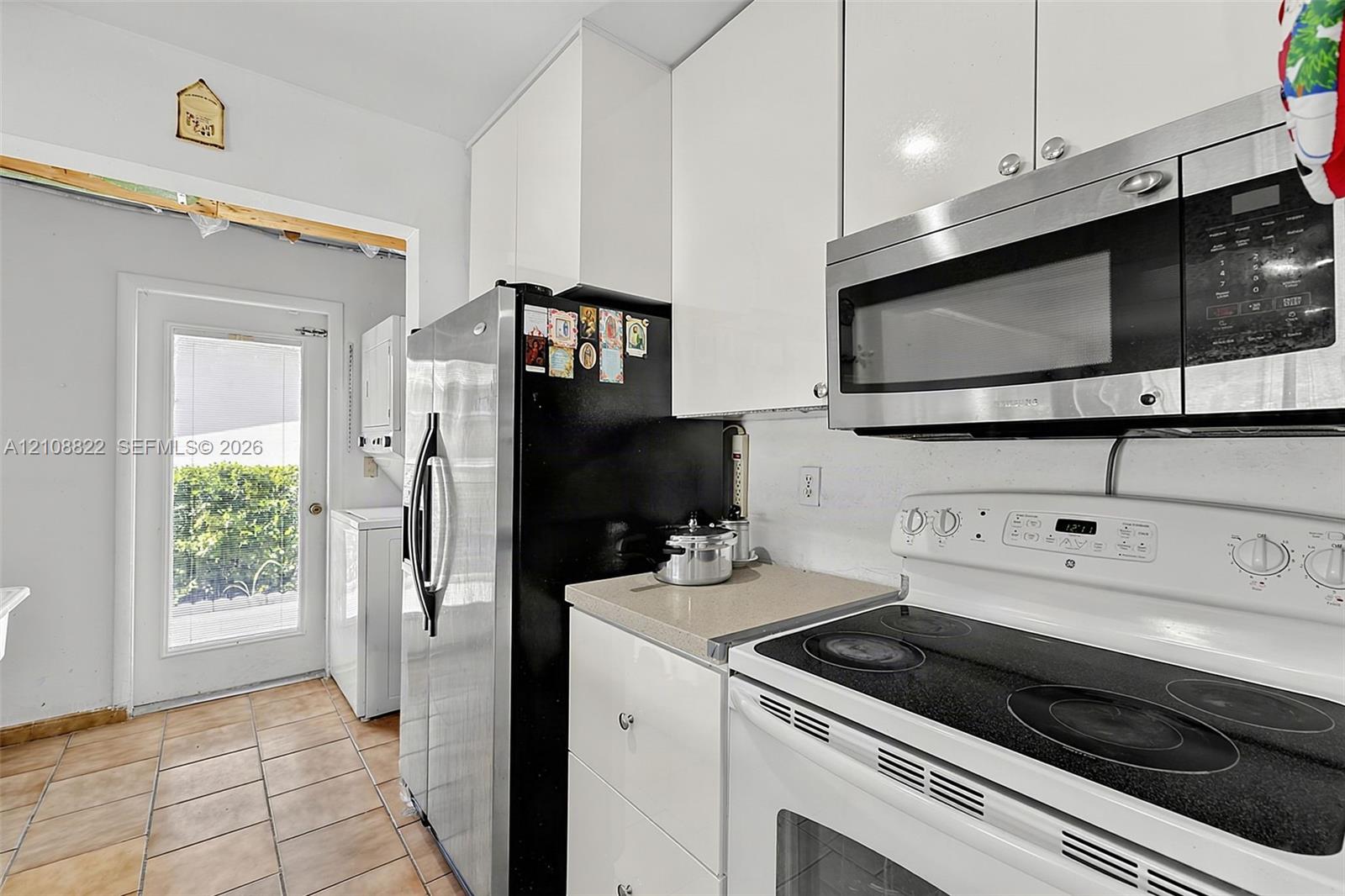 Kitchen featuring high-gloss white cabinetry, stone-finish countertops, ceramic tile flooring, and stainless steel and white appliances