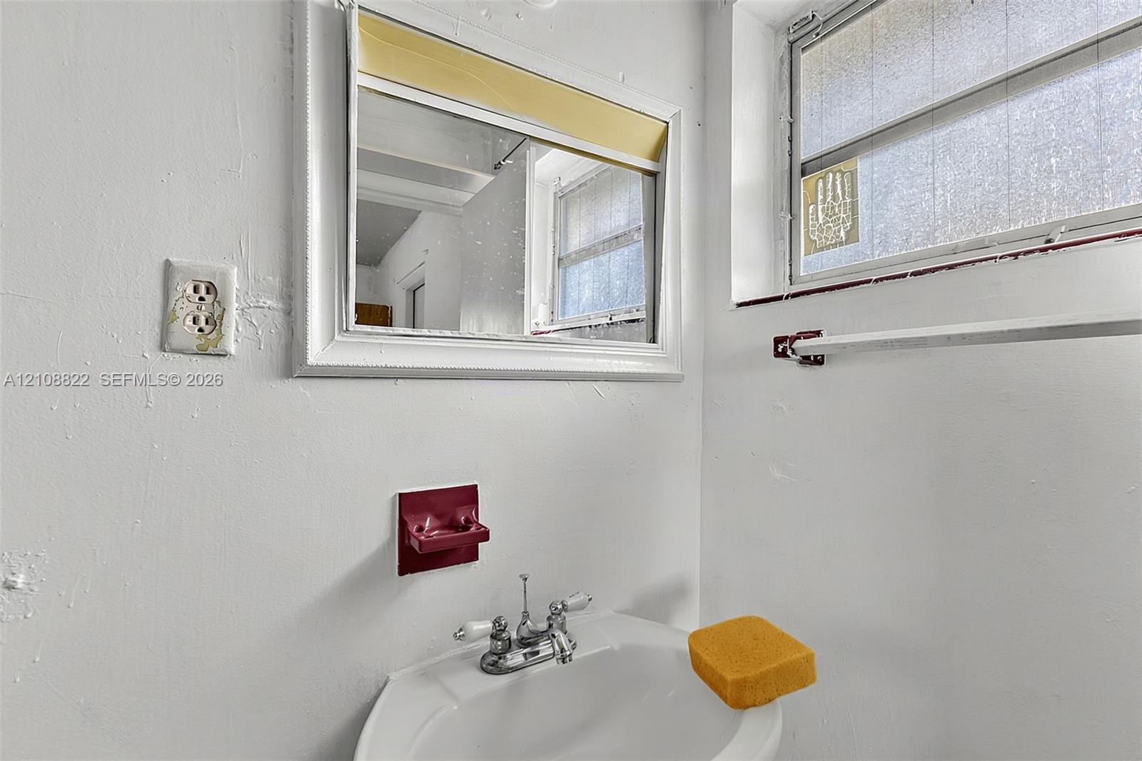 Wall-mounted sink basin with a chrome dual-handle faucet, framed wall mirror, and integrated towel bar