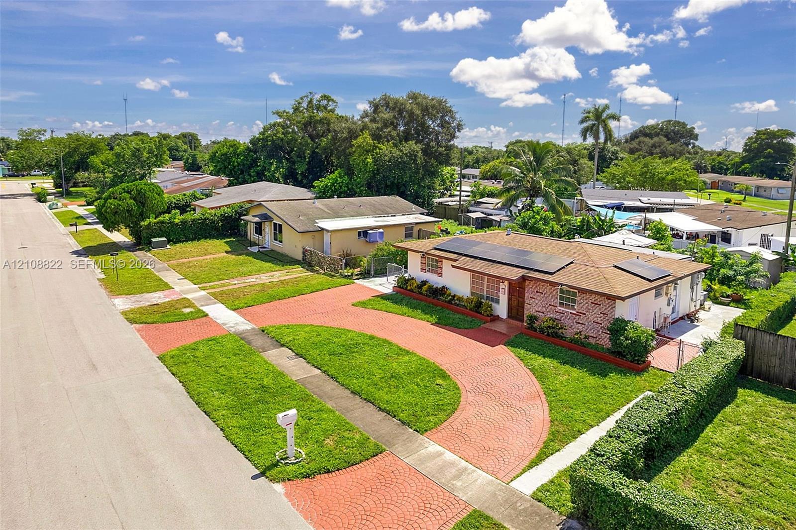Single-story residence featuring a brick and stucco exterior, roof-mounted solar panels, a circular paver driveway, and professional landscaping