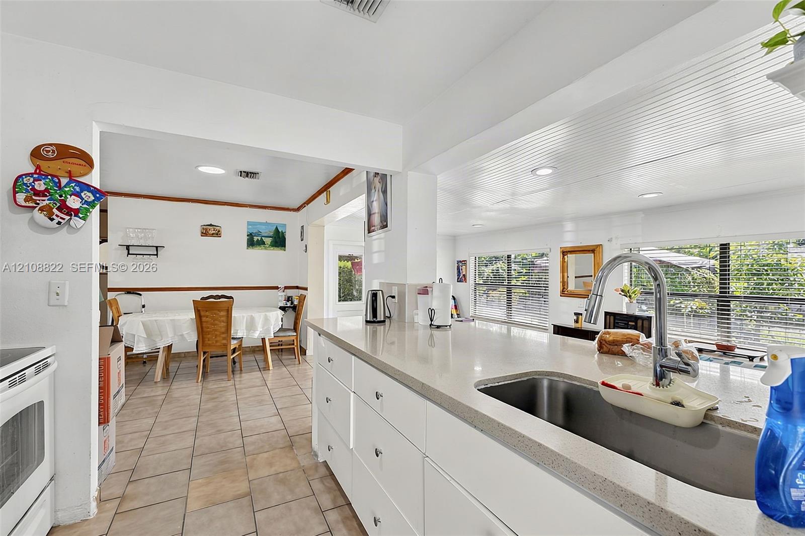 Kitchen featuring white cabinetry, solid-surface countertops, an undermount stainless steel sink with a high-arch pull-down faucet, recessed ceiling lighting, and ceramic tile flooring