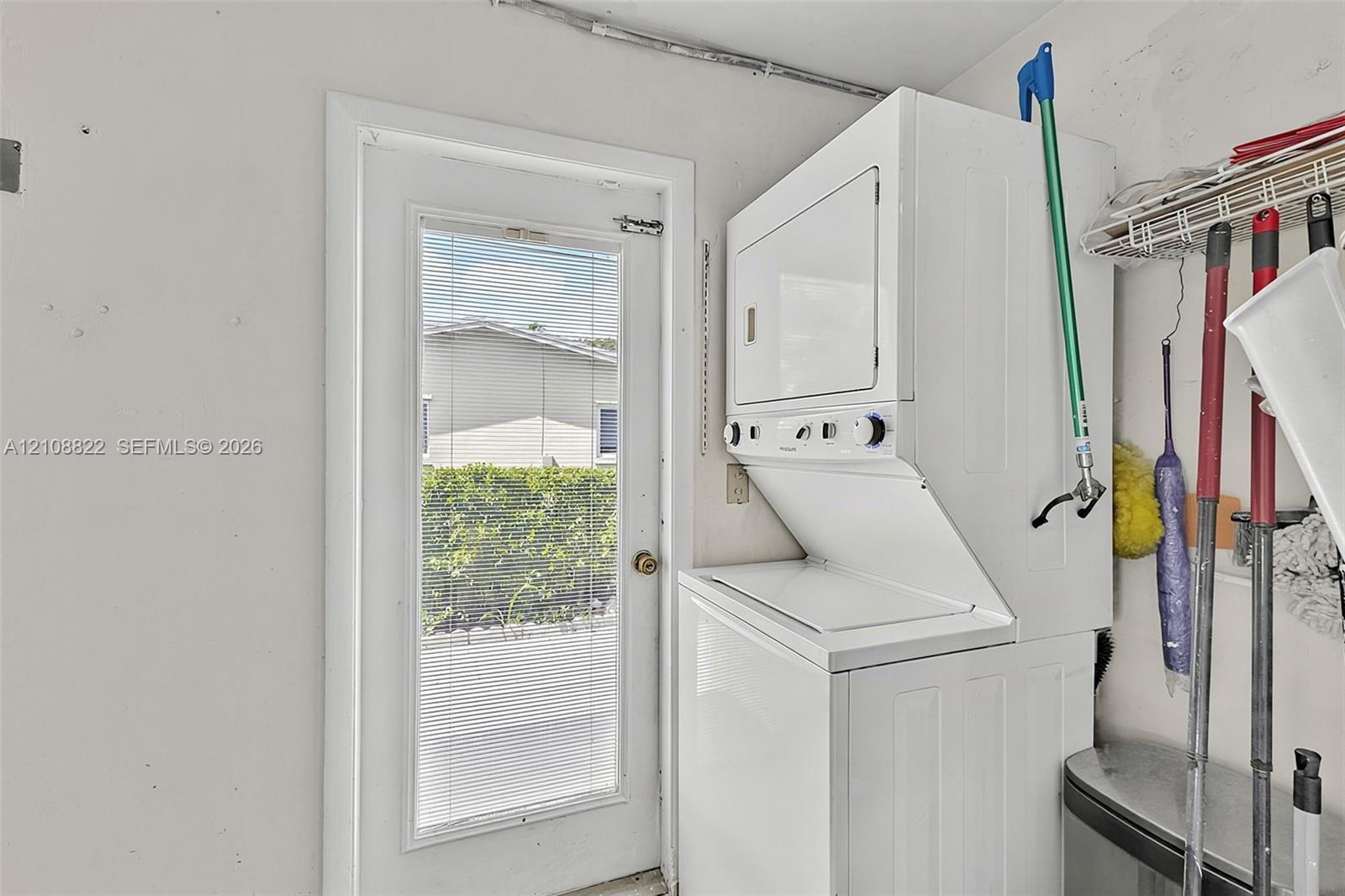 Stacked white laundry unit featuring front-loading controls and a full-lite exterior door with integrated blinds