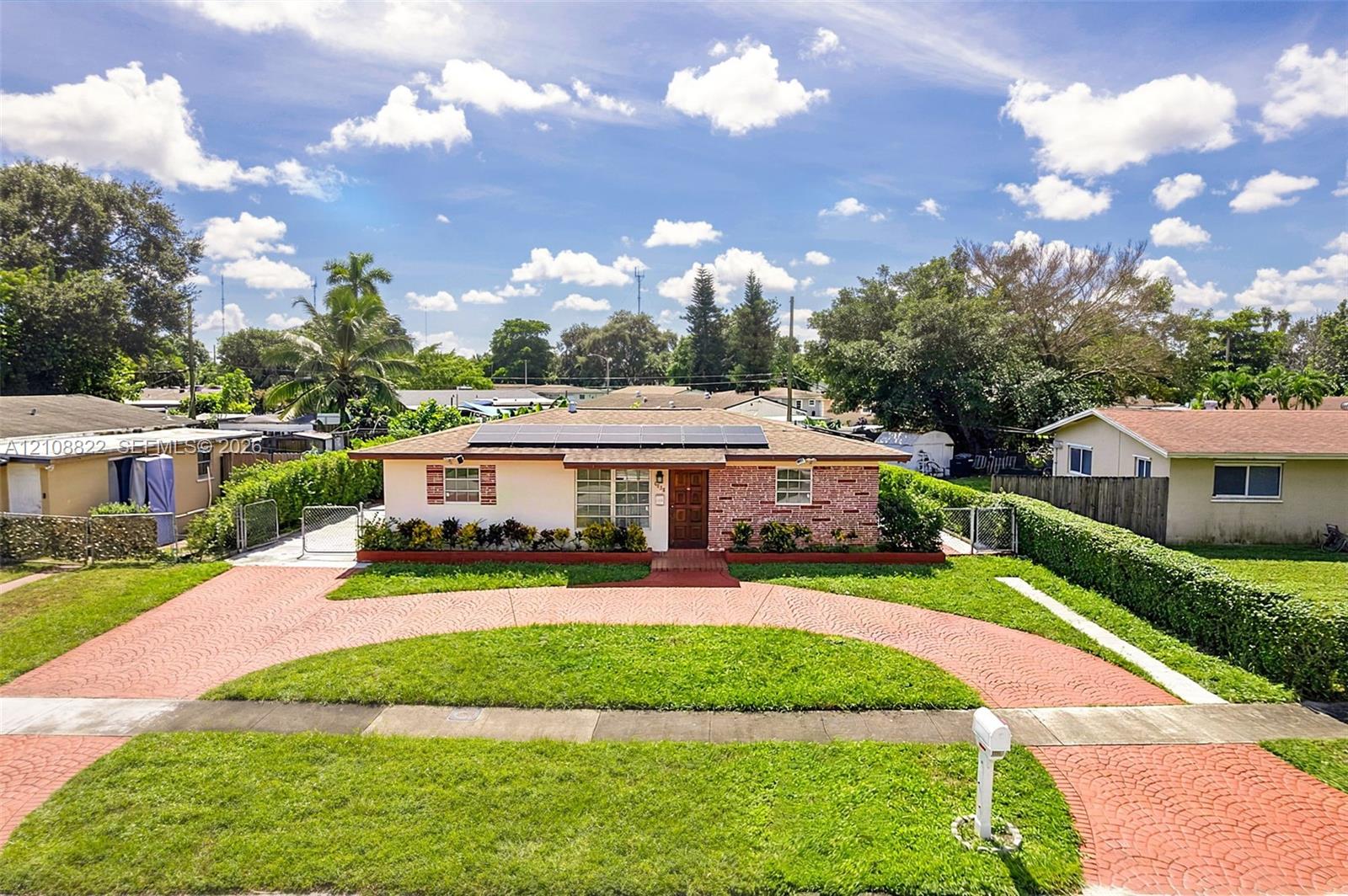 Single-story exterior featuring a brick facade, rooftop solar panels, a semi-circular paved driveway, and manicured landscaping