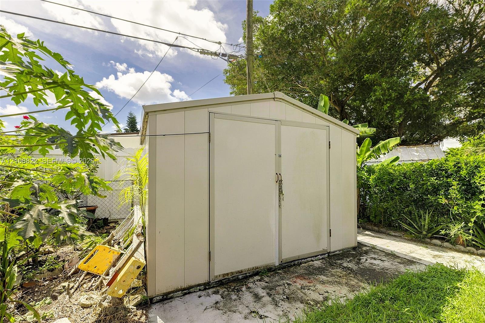 Detached metal storage structure featuring double doors and a gable roof, positioned on a concrete pad within the backyard