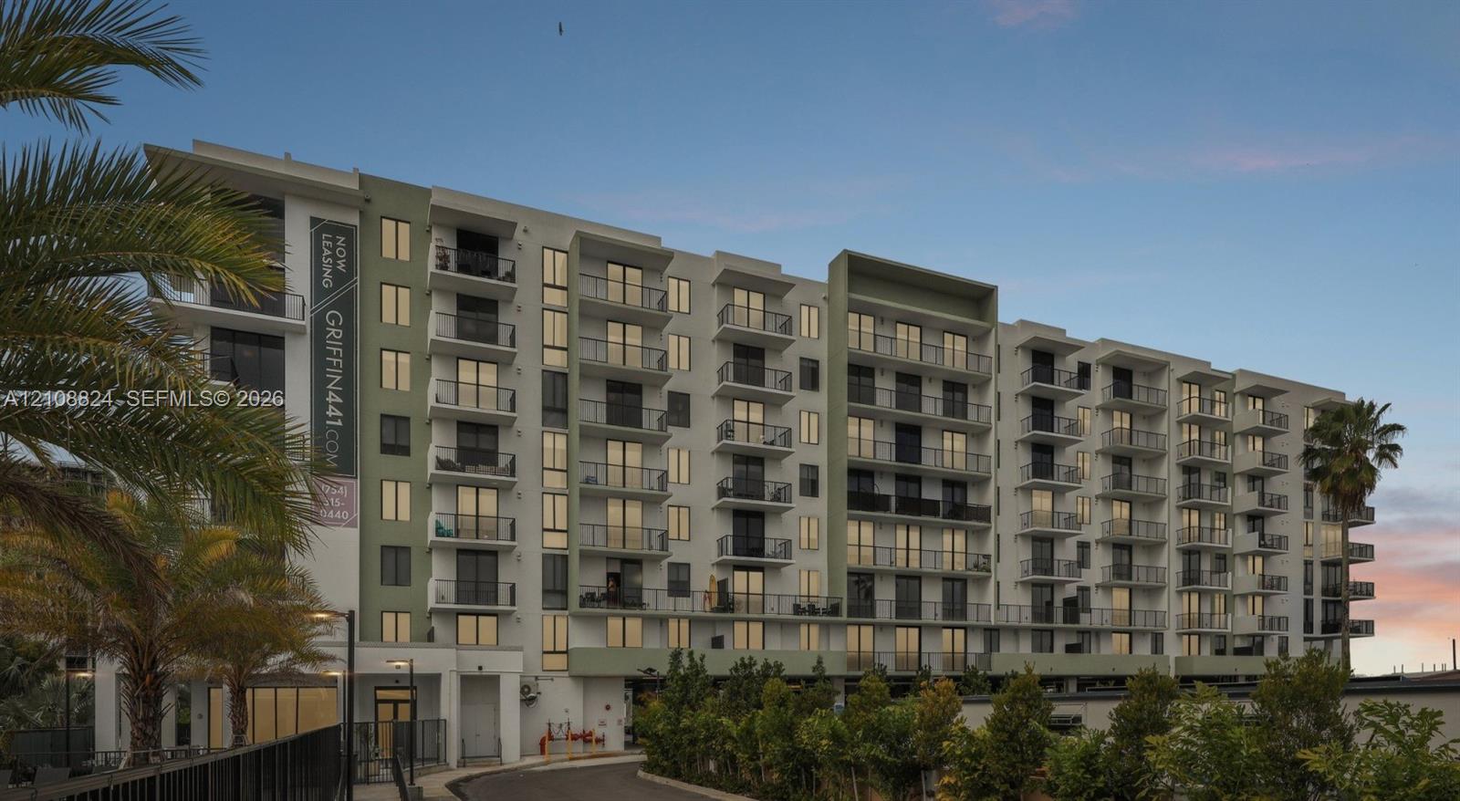 Multi-story residential building featuring a light-toned facade, recessed private balconies with metal railings, and integrated ground-level landscaping Multi-story residential building featuring a light-toned facade, recessed private balconies with metal railings, and integrated ground-level landscaping