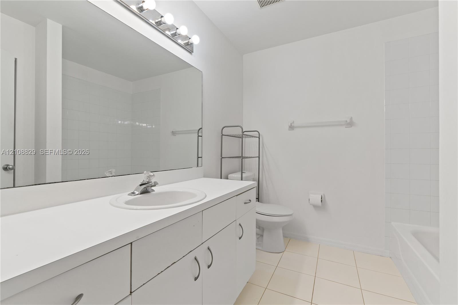 Bathroom featuring a vanity with a white countertop and oval sink, a large wall-mounted mirror, overhead multi-bulb lighting, and tile flooring