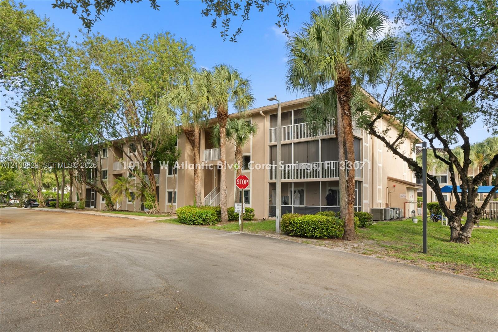 Multi-story residential building exterior featuring stucco cladding, screened balconies, and mature palm tree landscaping