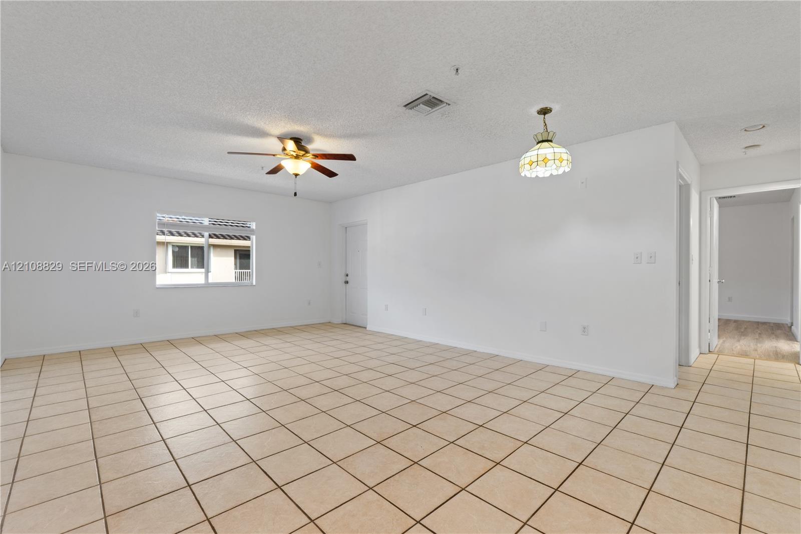Neutral tile flooring throughout, ceiling fan with integrated light fixture, decorative pendant light, and large window with natural light