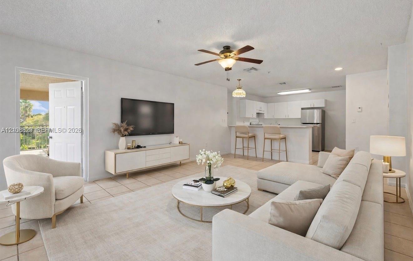 Open-concept living space featuring ceramic tile flooring, neutral wall tones, a ceiling fan, and a kitchen peninsula with bar seating