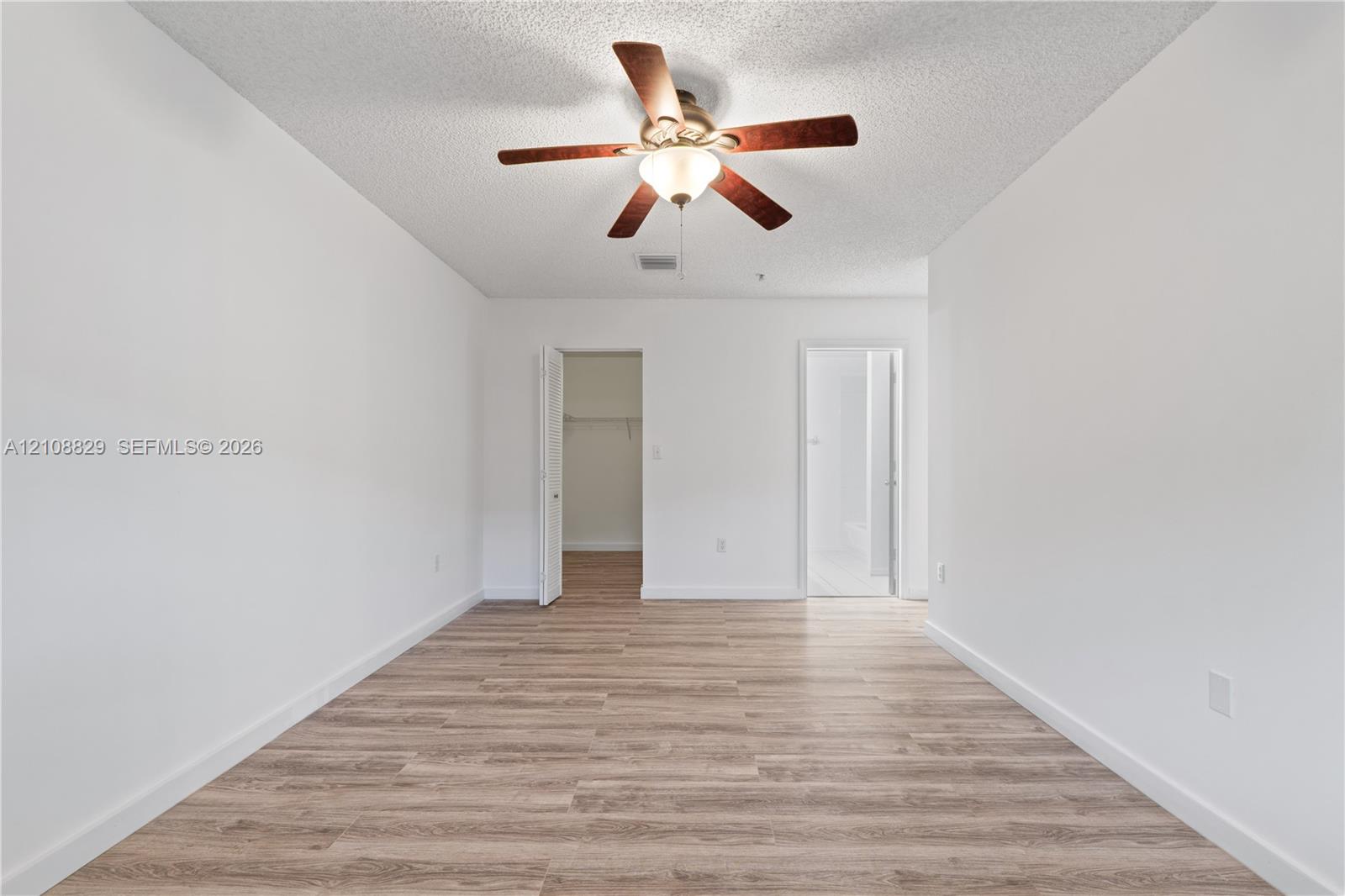 Room featuring wood-finish flooring, a ceiling fan with integrated lighting, and dual entry points to walk-in storage and an additional interior space