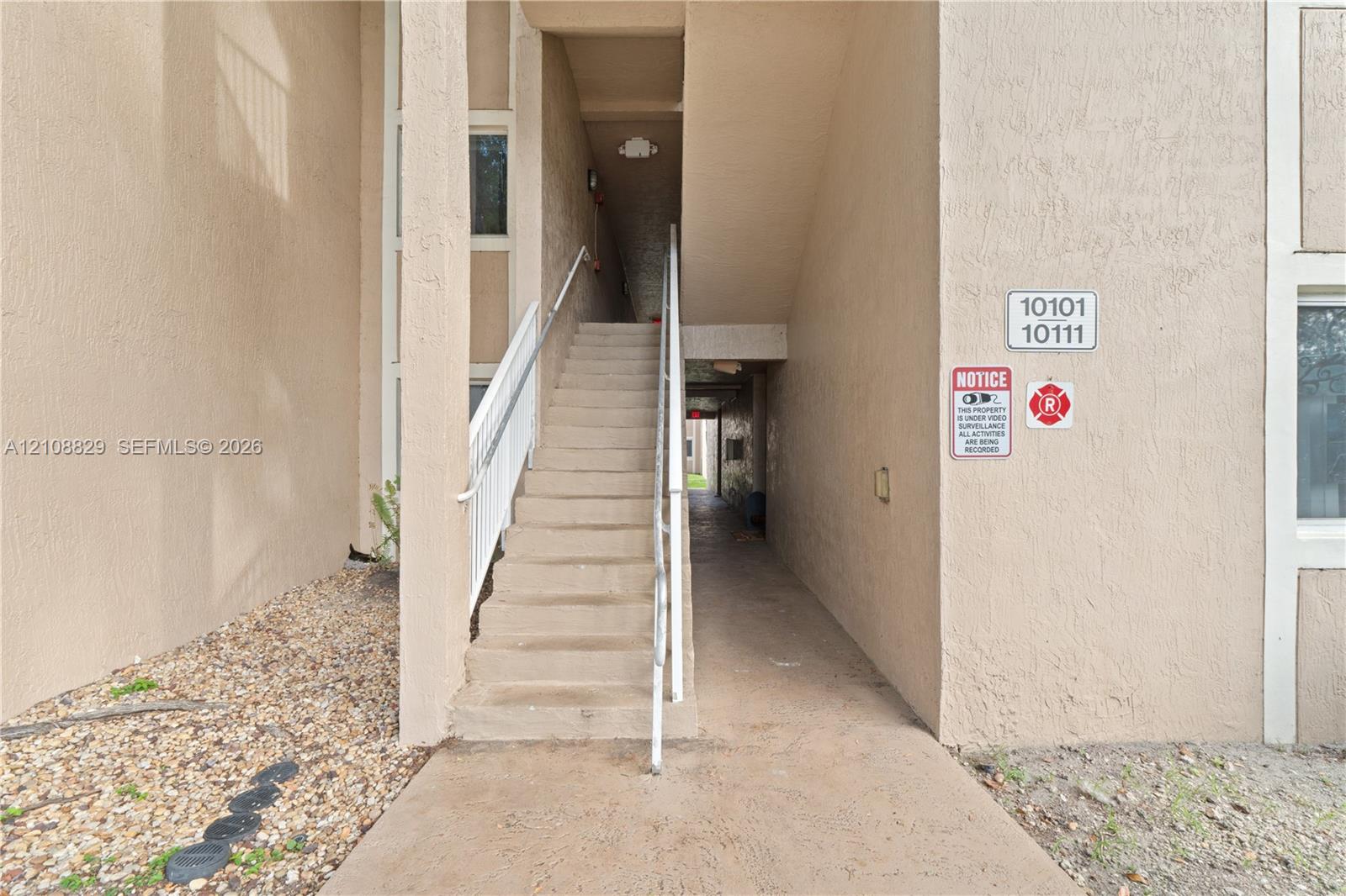 Stucco exterior facade featuring concrete stairs with white metal handrails, a concrete walkway, and built-in exterior lighting