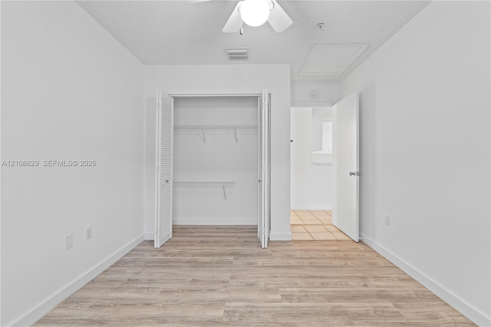 Room featuring wood-finish flooring, a ceiling fan with integrated lighting, and a closet with bifold louvered doors