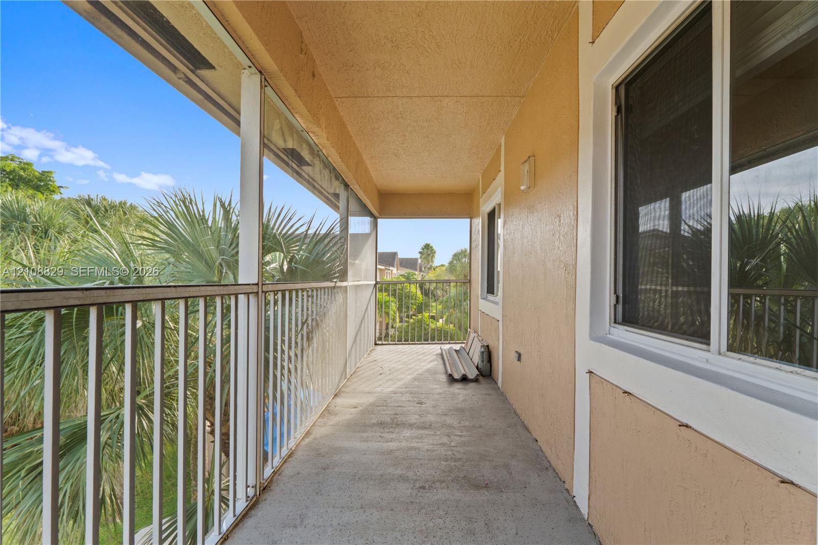 Covered balcony featuring screen enclosure, metal railing, concrete flooring, and exterior wall-mounted lighting
