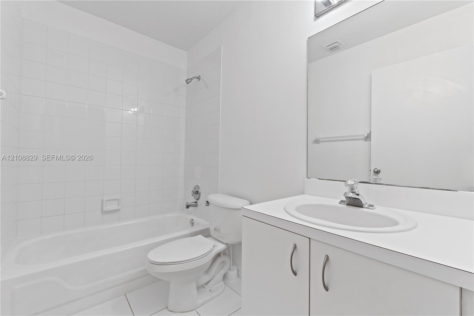 Bathroom featuring a white vanity cabinet with an integrated sink, a full-width wall mirror, a bathtub-shower combination with tile surround, and tile flooring