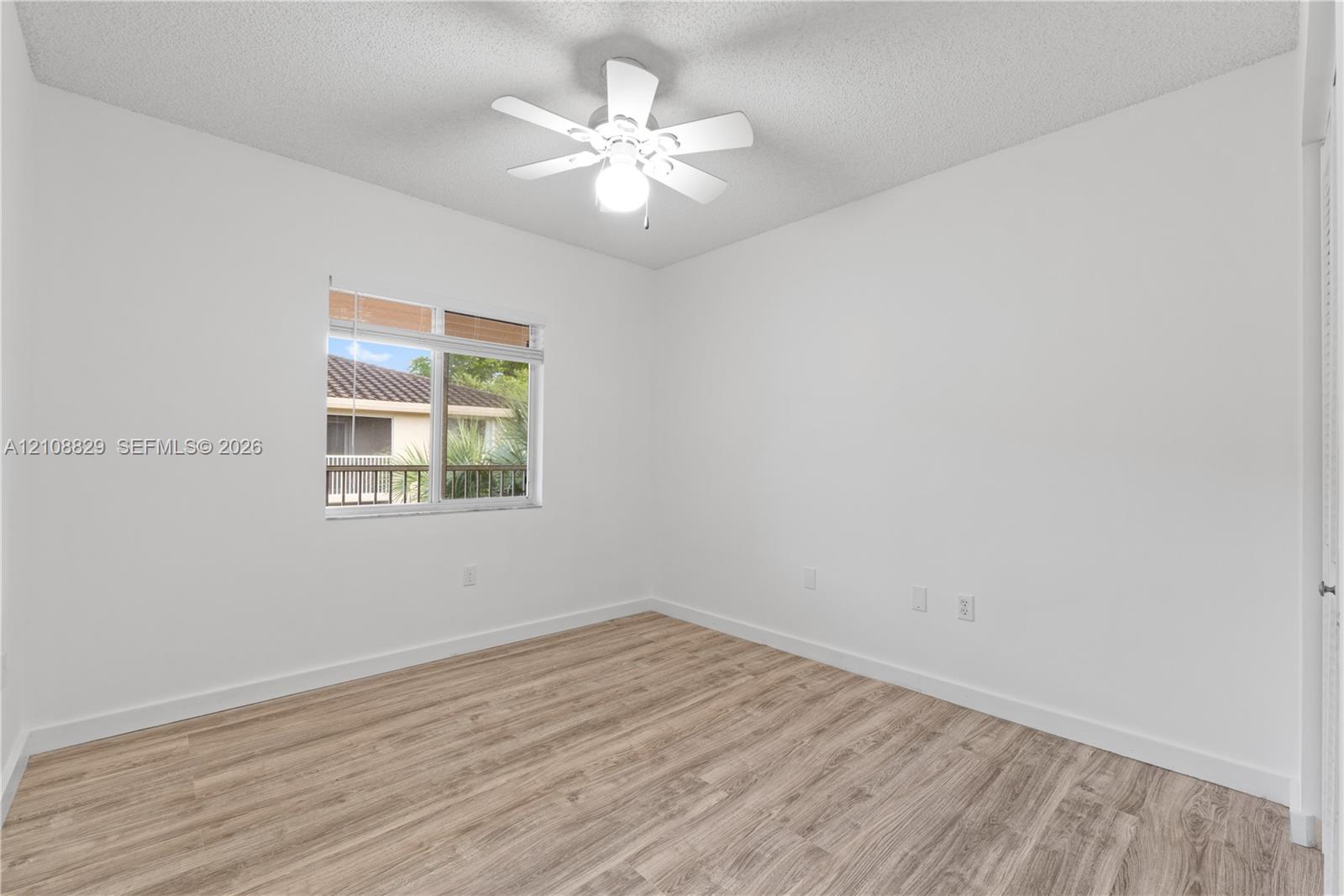 Room featuring wood-finish flooring, a white ceiling fan with integrated lighting, and a single-pane window