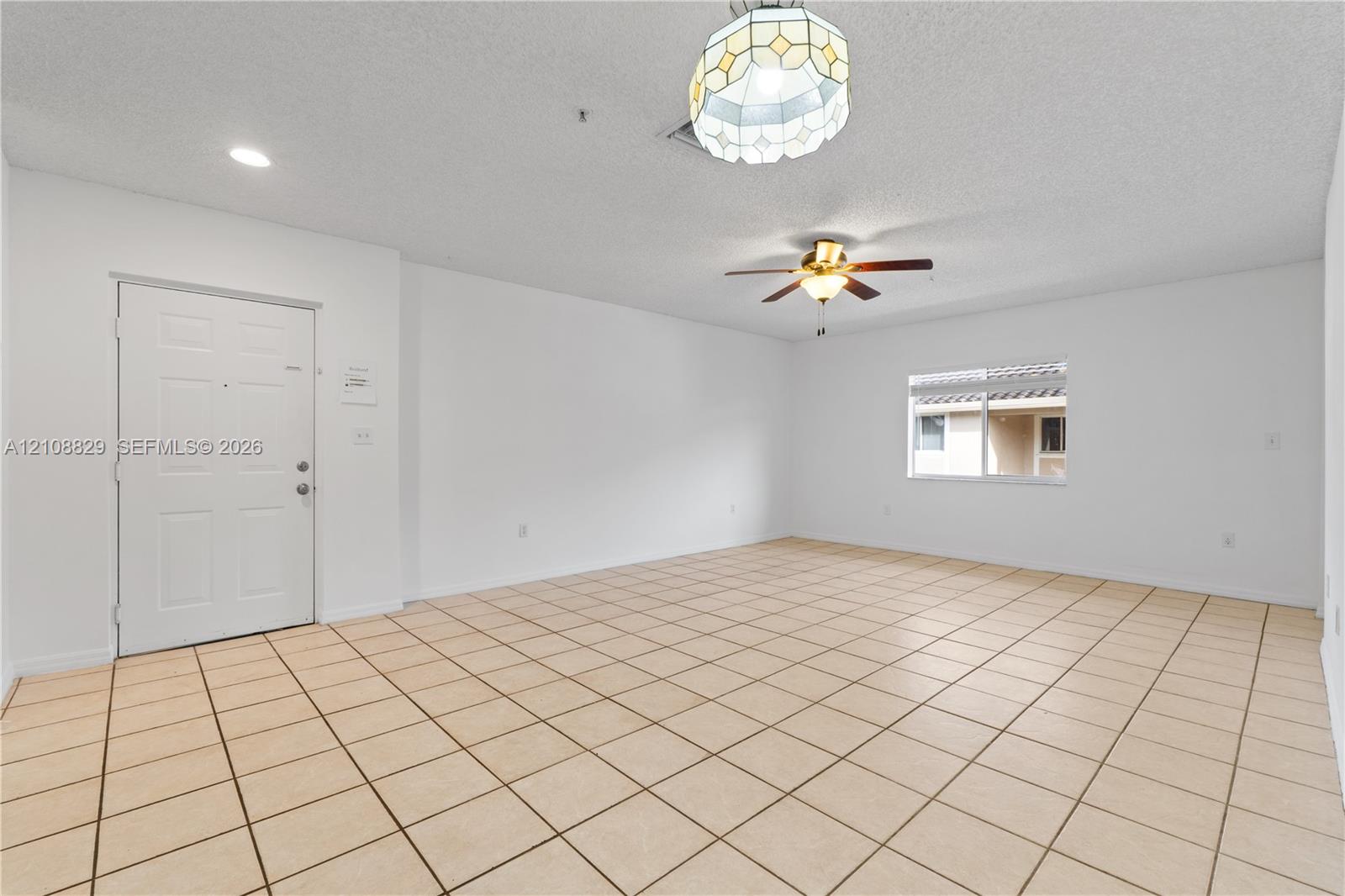 Neutral-toned tile flooring, ceiling fan with light fixture, decorative overhead pendant light, and textured ceiling