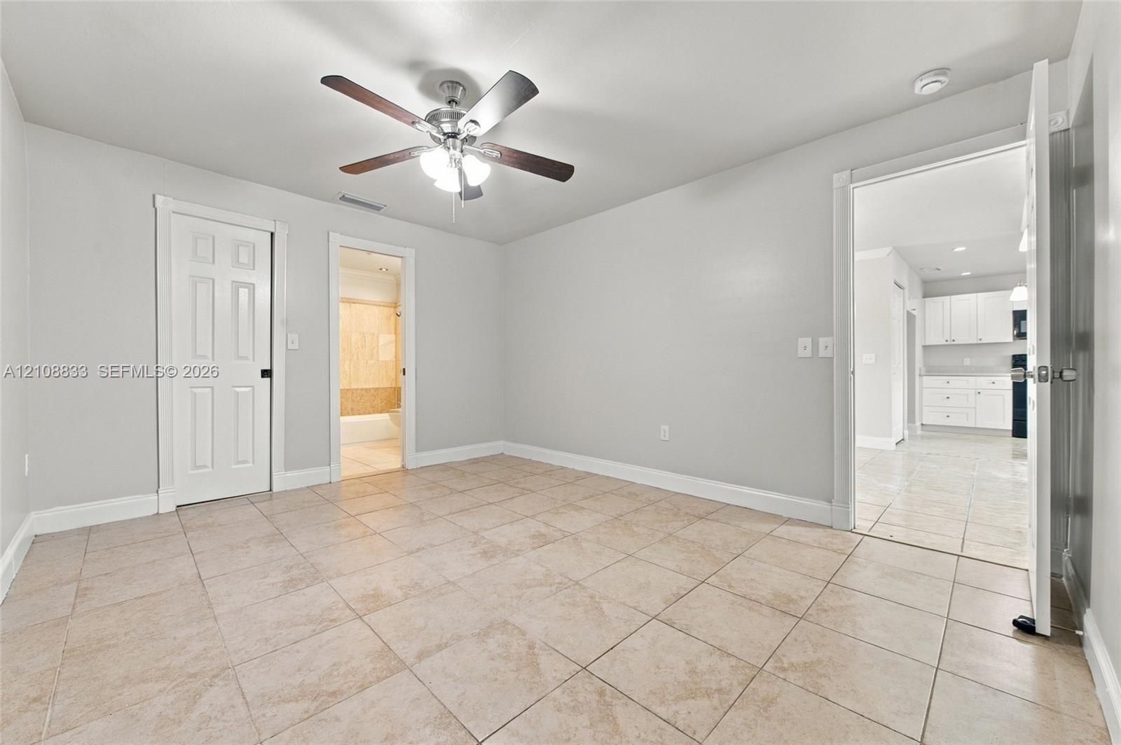 Neutral-toned interior featuring ceramic tile flooring, a central ceiling fan with integrated lighting, and white six-panel doors