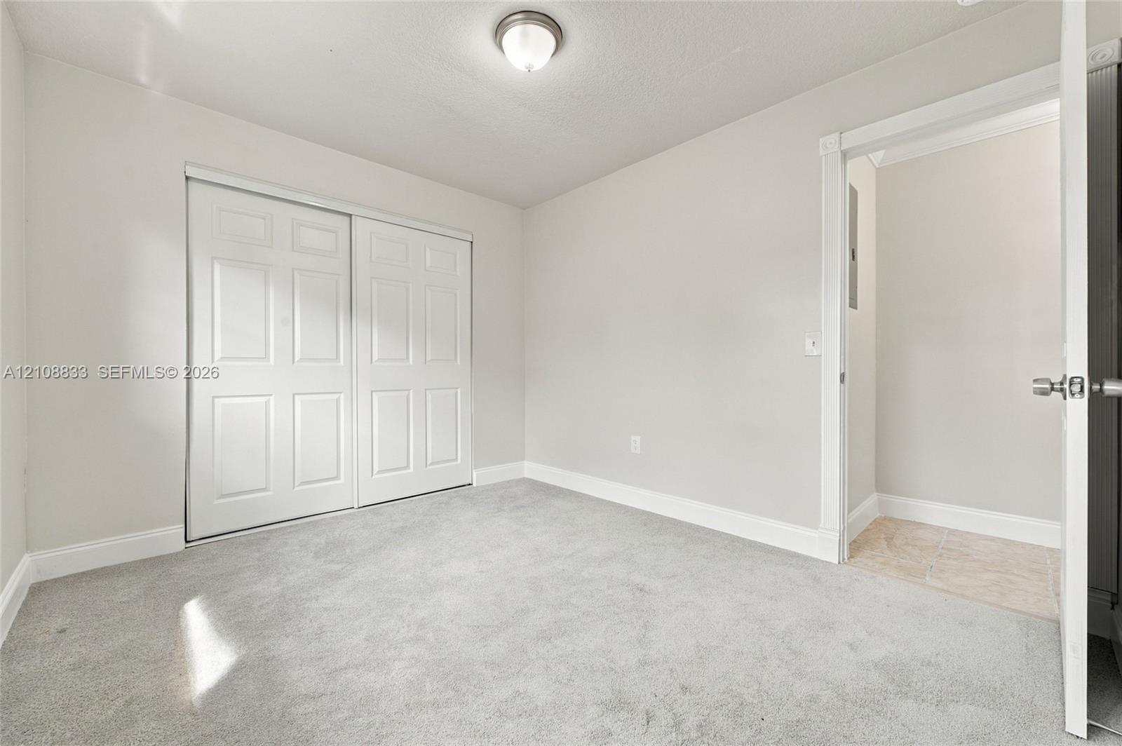 Neutral-toned carpeting, sliding panel closet doors, ceiling-mounted flush light fixture, and interior door with brushed metal hardware