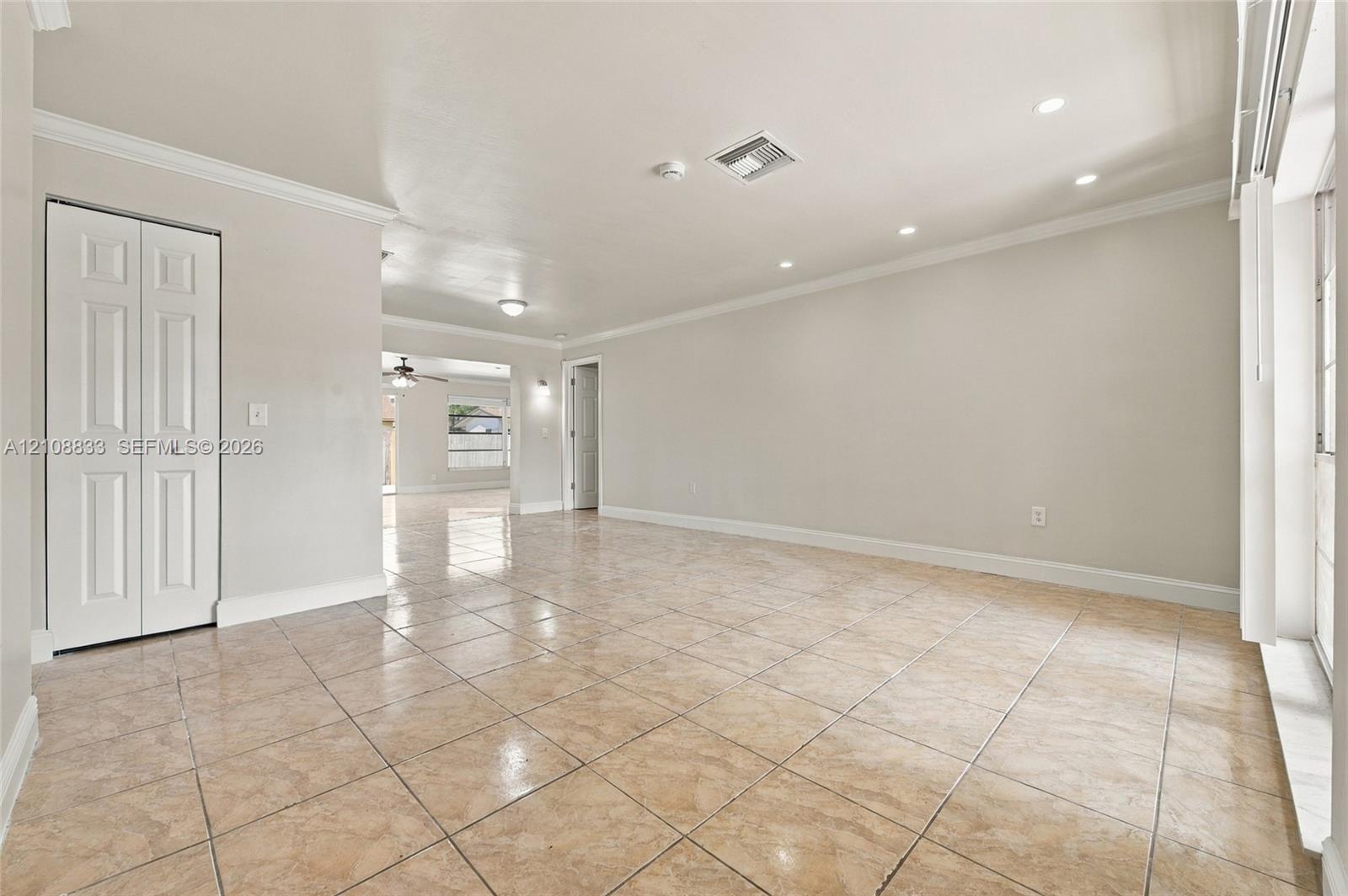 Interior room featuring neutral wall paint, recessed lighting, crown molding, tile flooring, and a closet with paneled doors