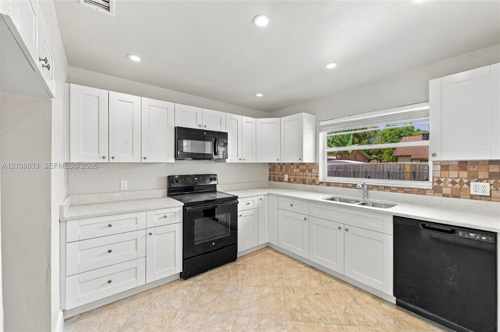 Kitchen featuring white cabinetry, solid surface countertops, a tiled backsplash, black built-in appliances, and recessed lighting