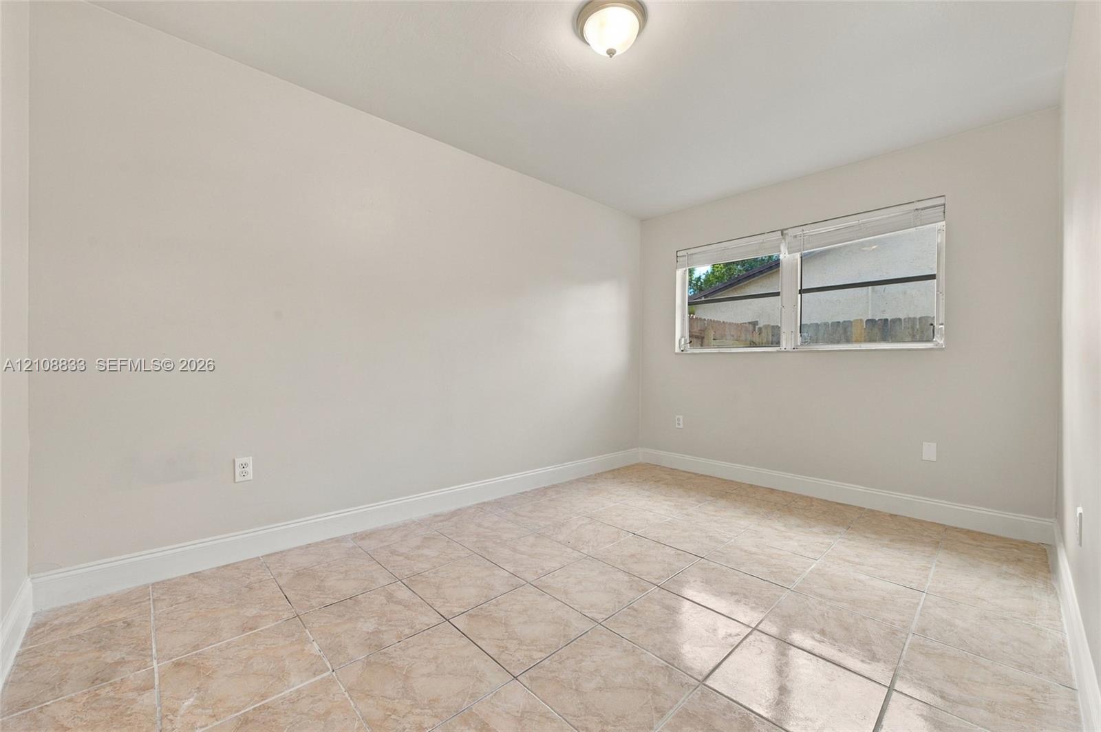 Neutral-toned interior space featuring large-format tile flooring, a dual-pane horizontal sliding window, and a ceiling-mounted flush light fixture
