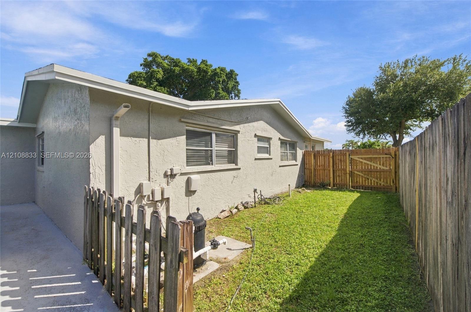 Exterior side yard featuring stucco siding, horizontal sliding windows, a manicured lawn, and wood privacy fencing with an integrated gate