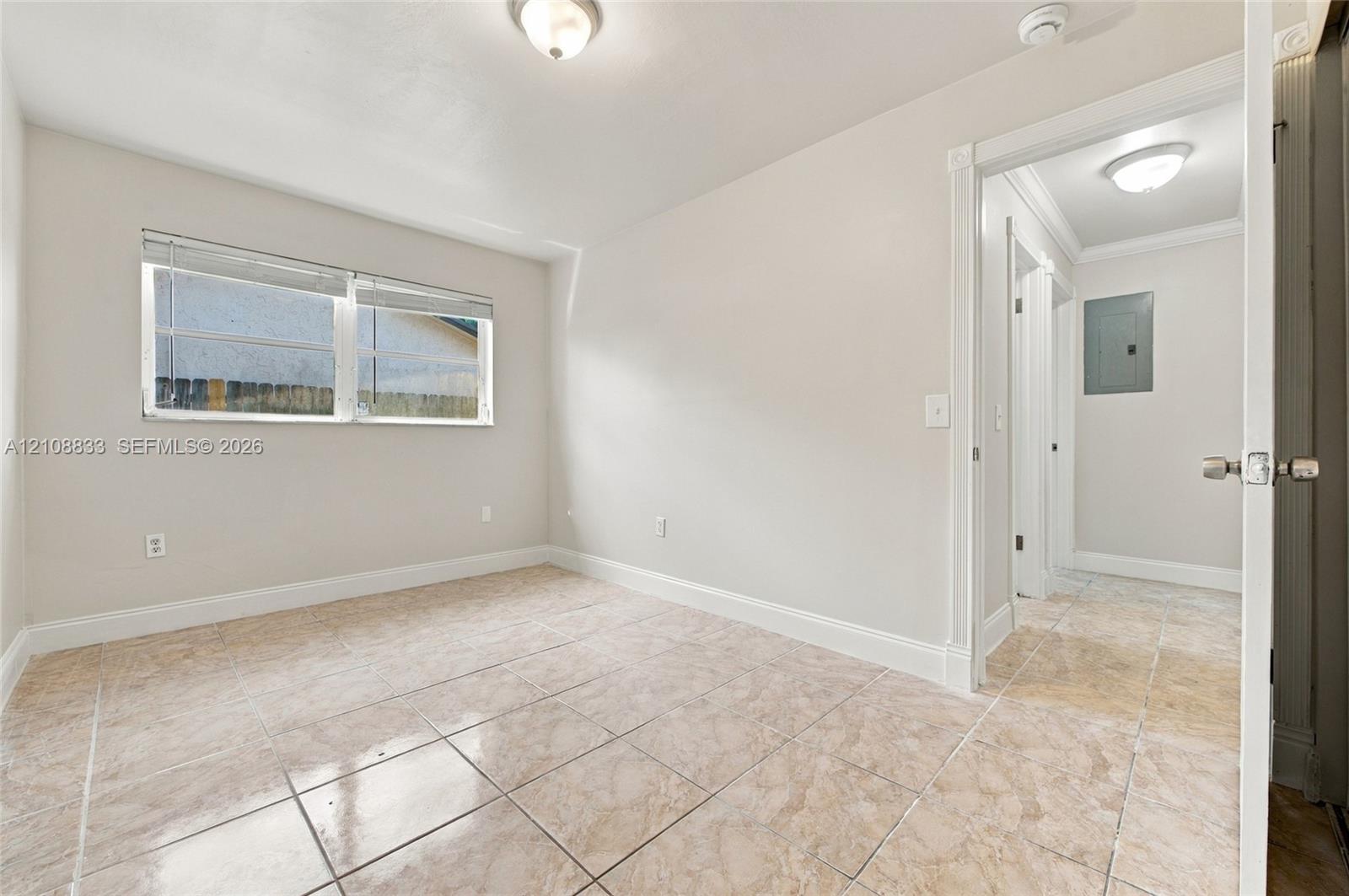 Neutral-toned interior room featuring tile flooring, a dual-pane sliding window with horizontal blinds, and overhead lighting