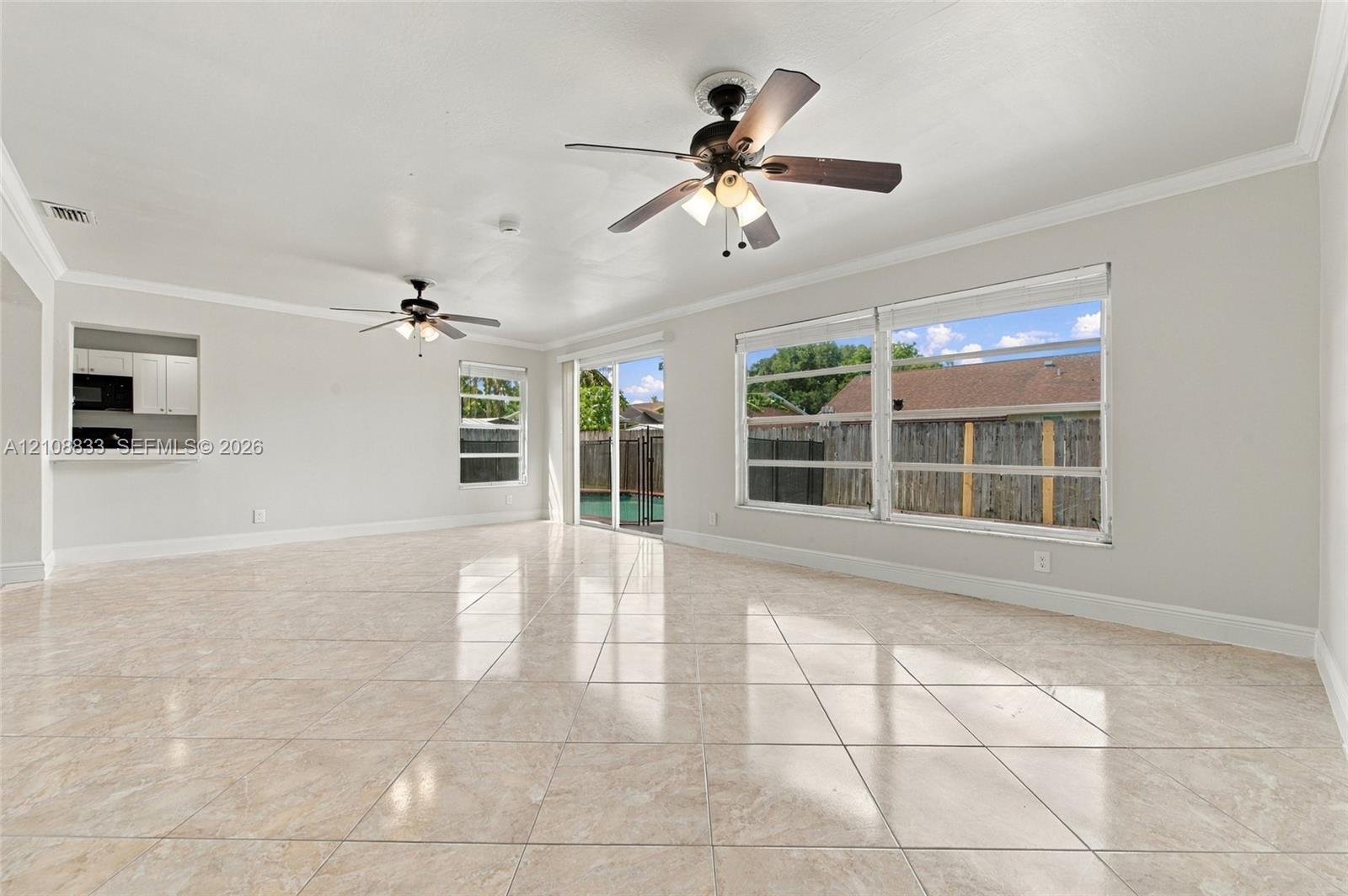 Interior space featuring large-format tile flooring, two ceiling fans with integrated light kits, crown molding, and sliding glass doors