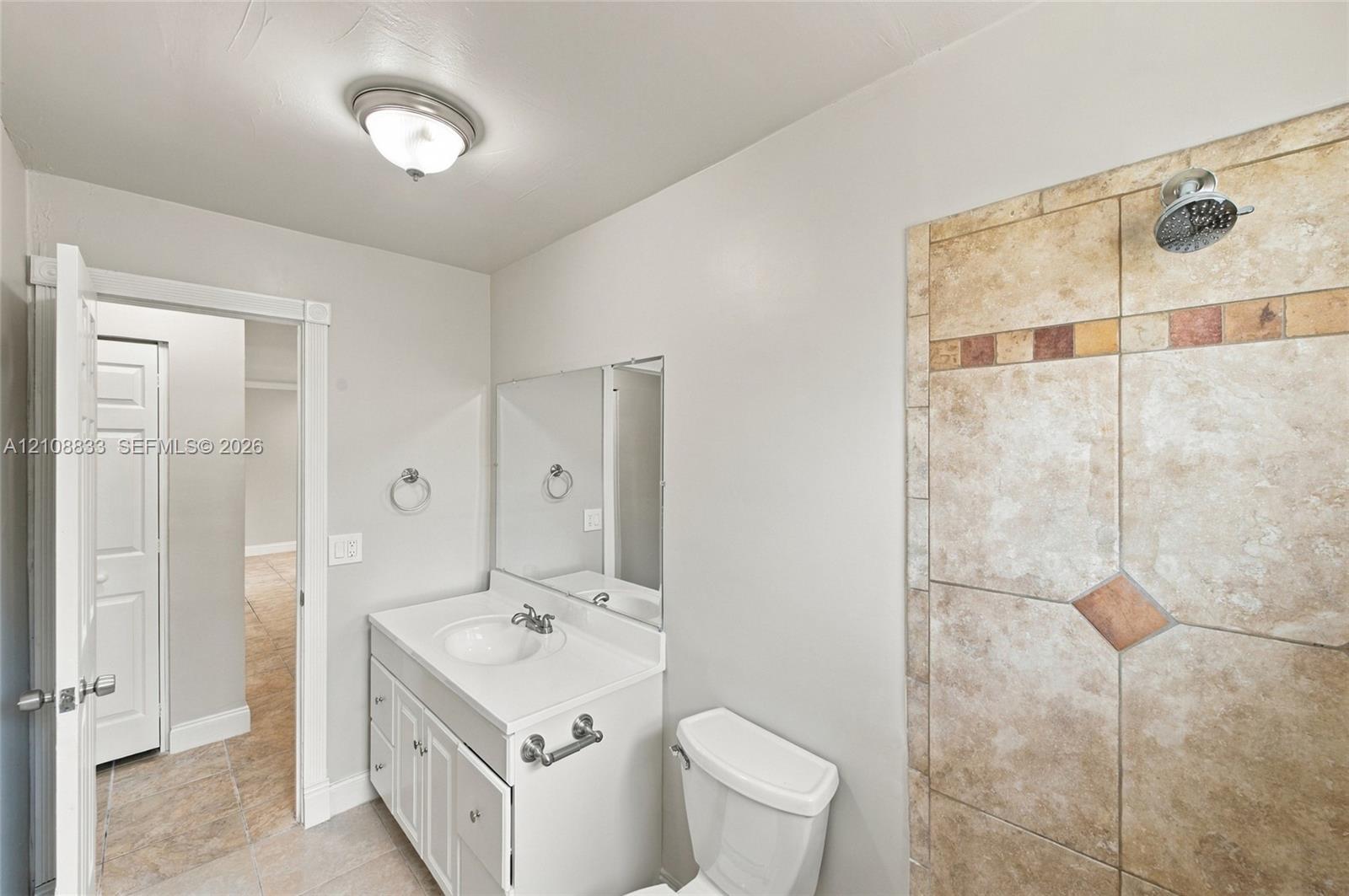 Bathroom featuring white cabinetry, integrated sink, wall-mounted mirror, and tile-surround shower with decorative stone-finish accents