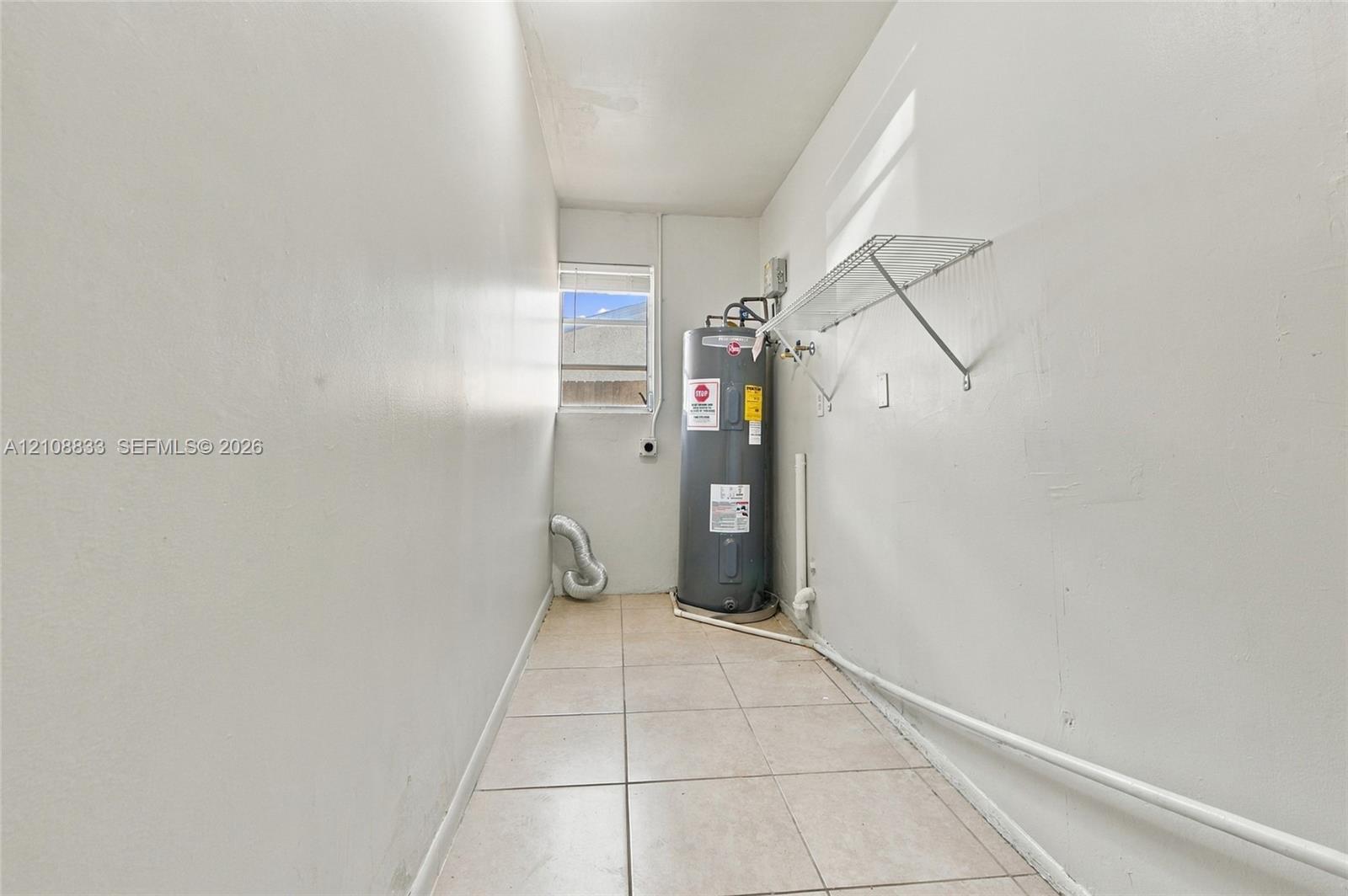 Utility space featuring light-toned tile flooring, a window, wall-mounted wire shelving, and an installed water heater
