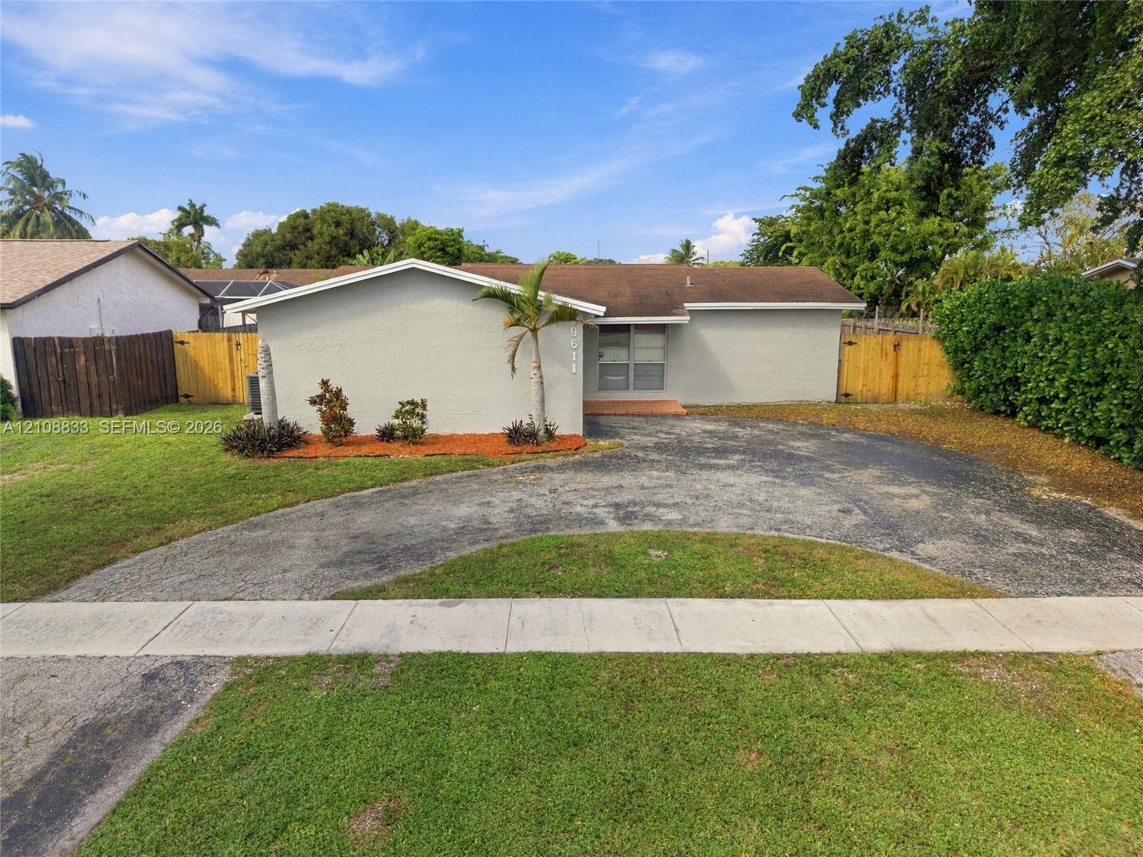 Single-story residence featuring a low-slope roof, textured exterior finish, circular paved driveway, and wood-panel fencing