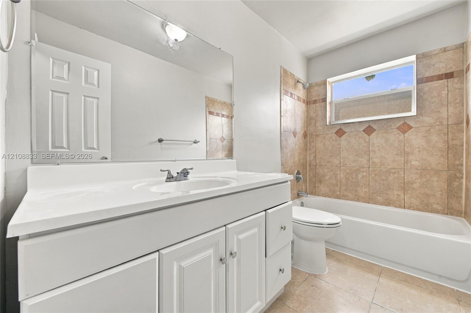 Bathroom featuring a white vanity with an integrated sink, a full-width mirror, tile flooring, and a bathtub with decorative tile surround