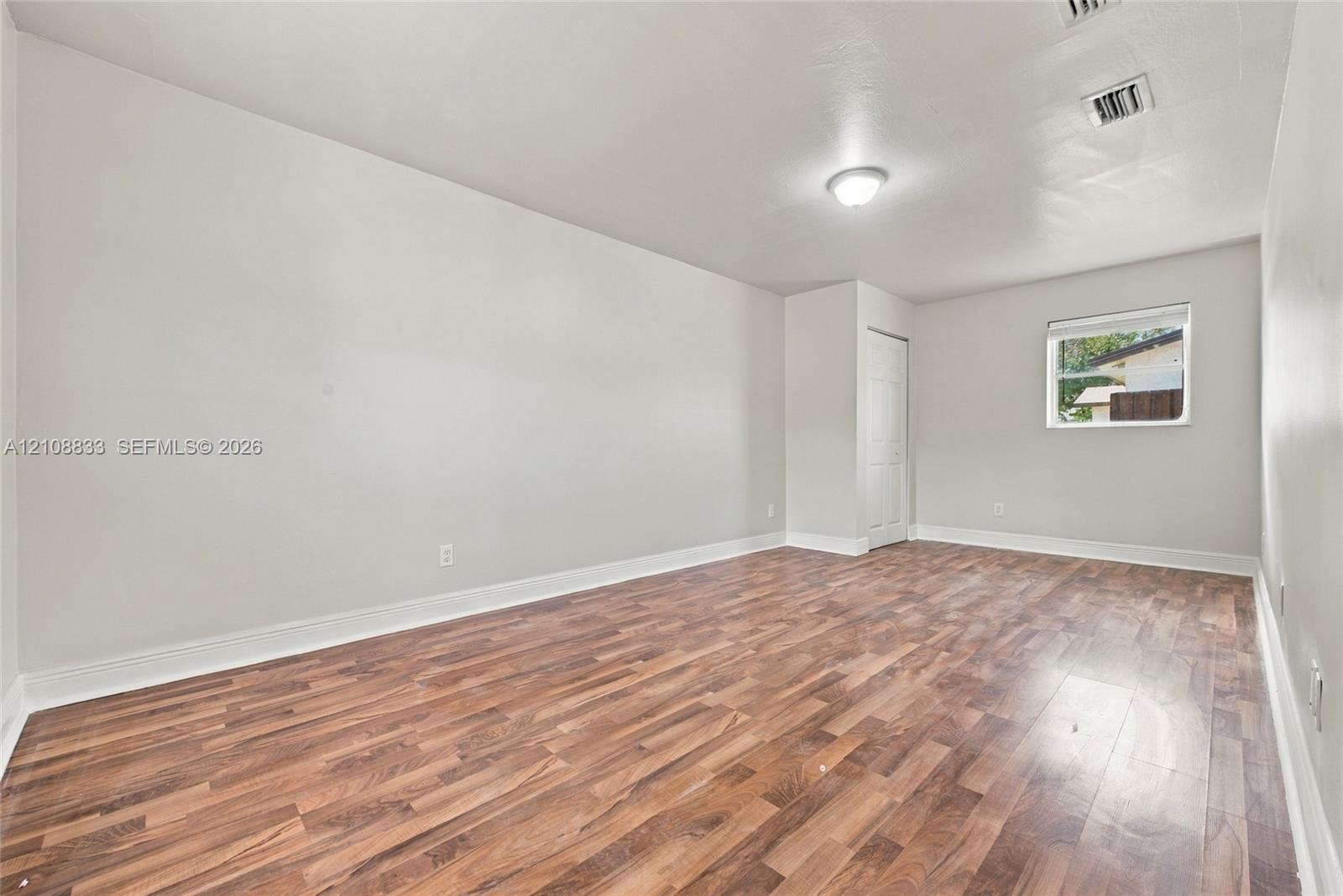 Interior room featuring wood-finish flooring, a single-pane window, flush-mount ceiling lighting, and a paneled closet door