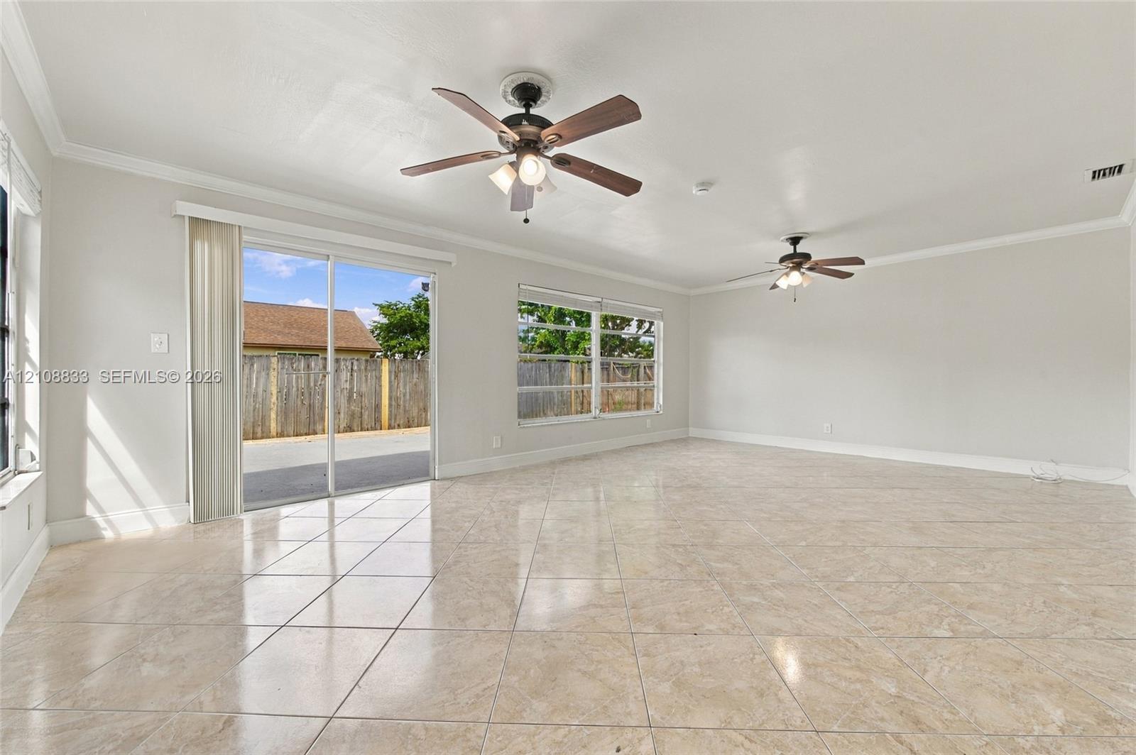Spacious room featuring large-format tile flooring, dual ceiling fans with integrated lighting, and sliding glass doors