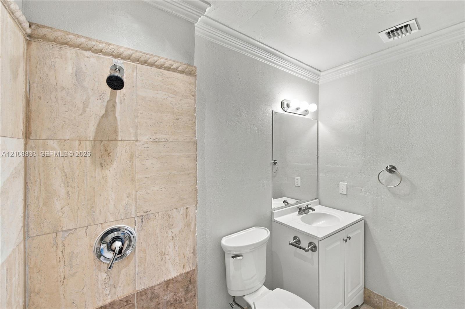 Bathroom featuring stone-tiled shower walls with a decorative rope-style border, white vanity cabinetry with a stone countertop, an integrated sink, and polished chrome hardware