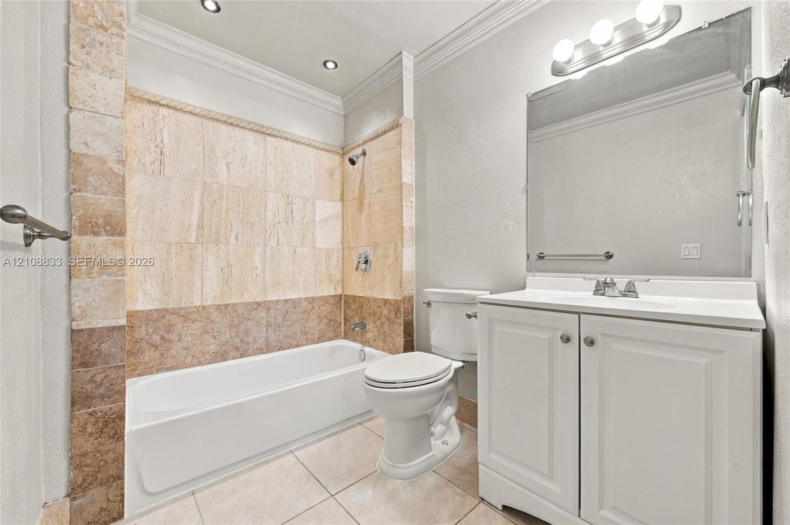 Bathroom featuring a tub-shower combination with multi-toned stone tile surround, vanity with cabinetry, large-format mirror, and crown molding