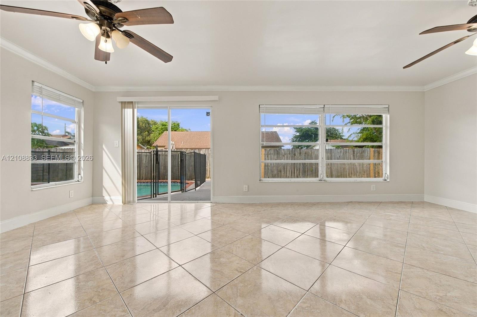 Neutral-toned interior featuring large-format tile flooring, dual ceiling fans with integrated light fixtures, and expansive windows
