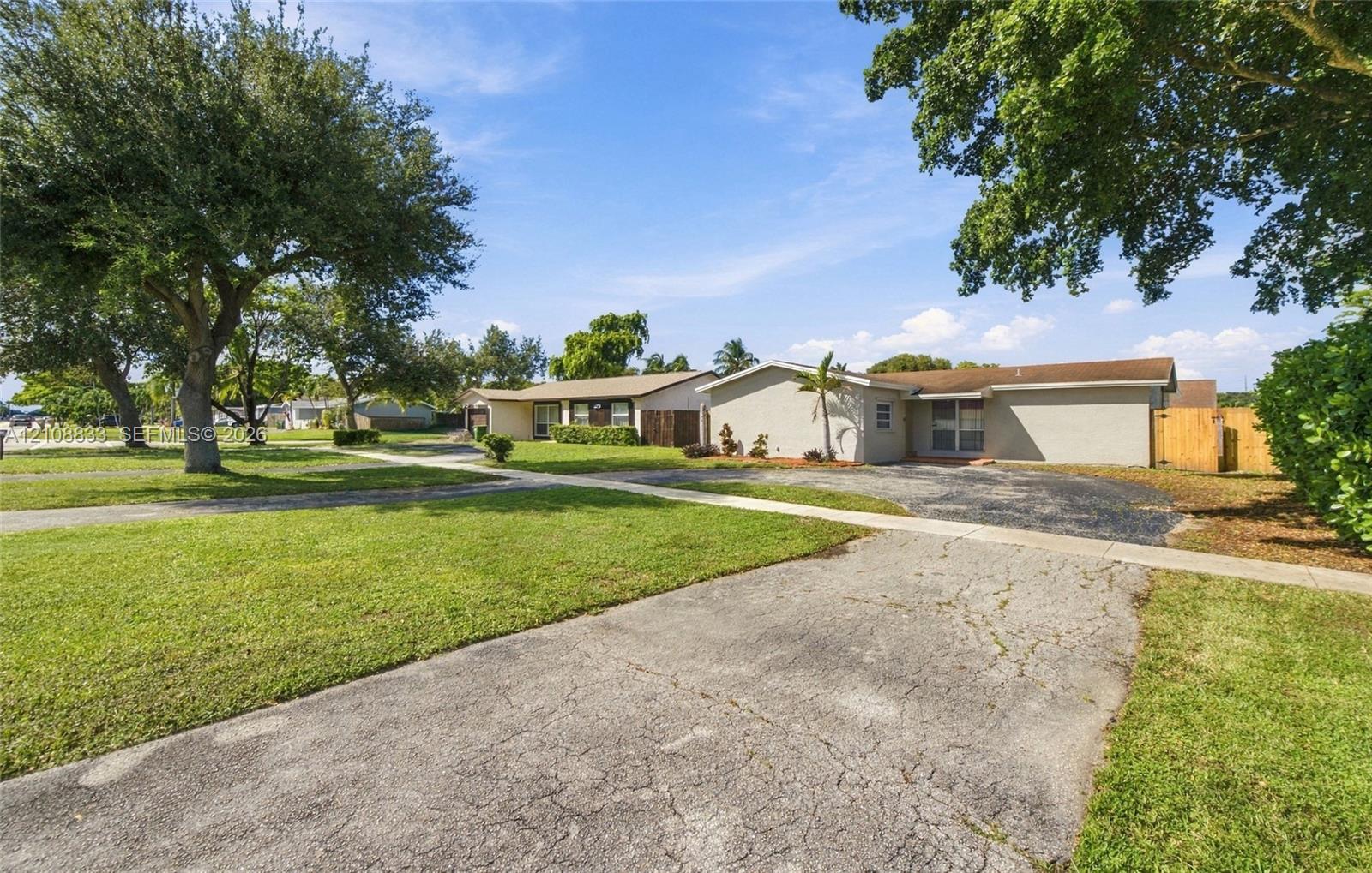 Single-story exterior featuring a stucco facade, expansive front lawn, mature trees, and a paved driveway