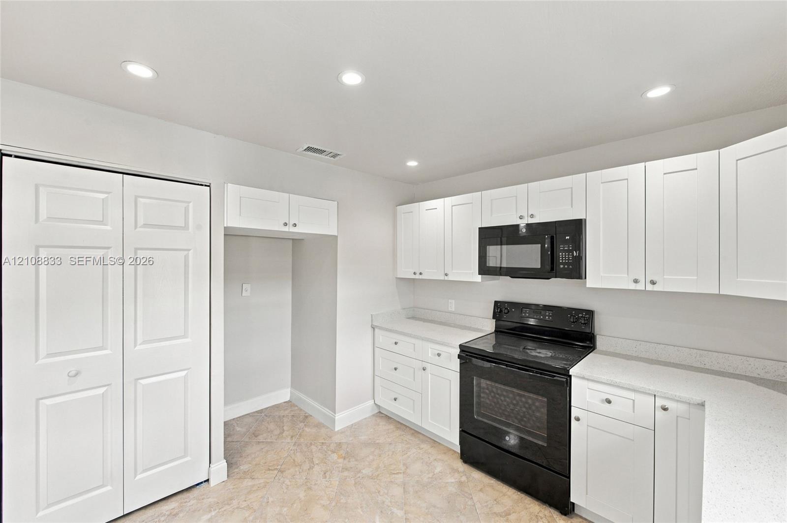 Kitchen featuring white shaker-style cabinetry, solid-surface countertops, black range with matching over-the-range microwave, and tile flooring