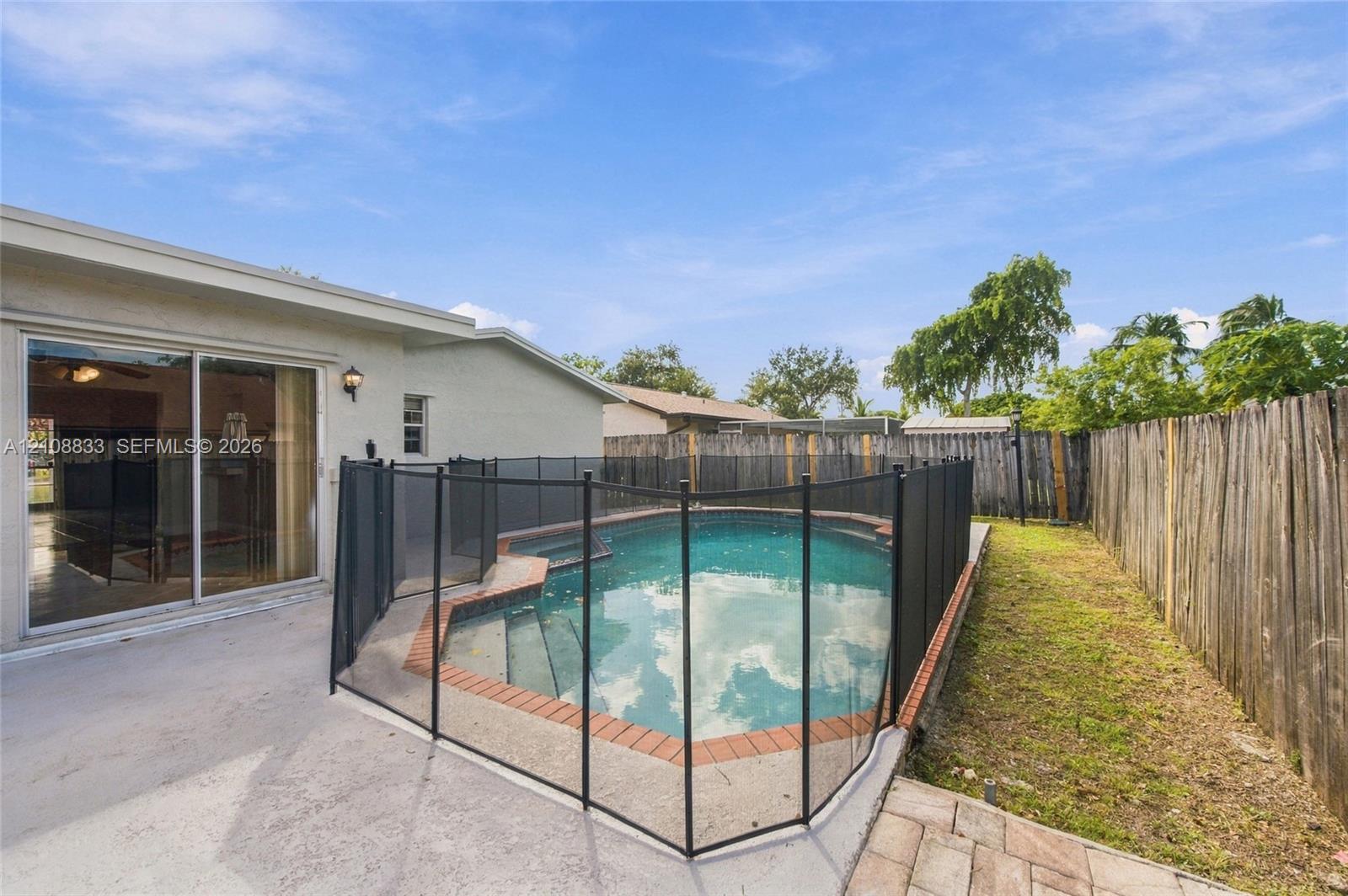 Backyard featuring an in-ground swimming pool with brick coping, a protective mesh safety fence, a concrete patio, and a wood privacy fence