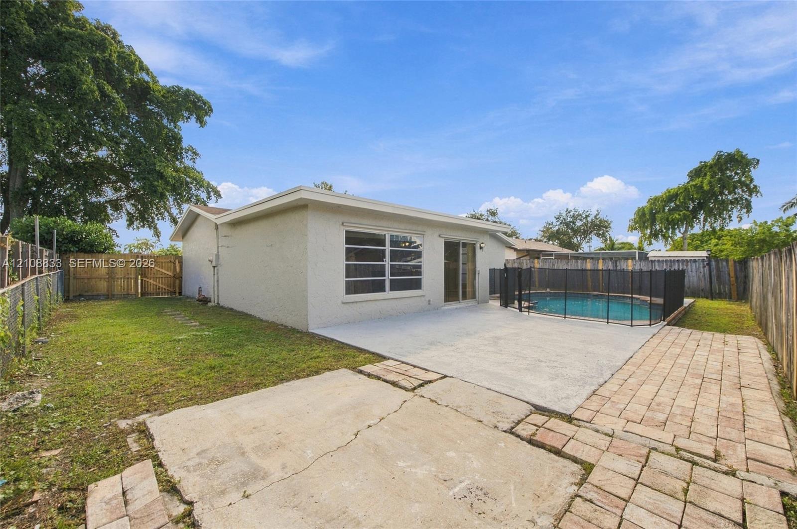 Backyard featuring an in-ground pool with mesh safety fencing, a concrete patio, brick paver accents, and wood perimeter fencing