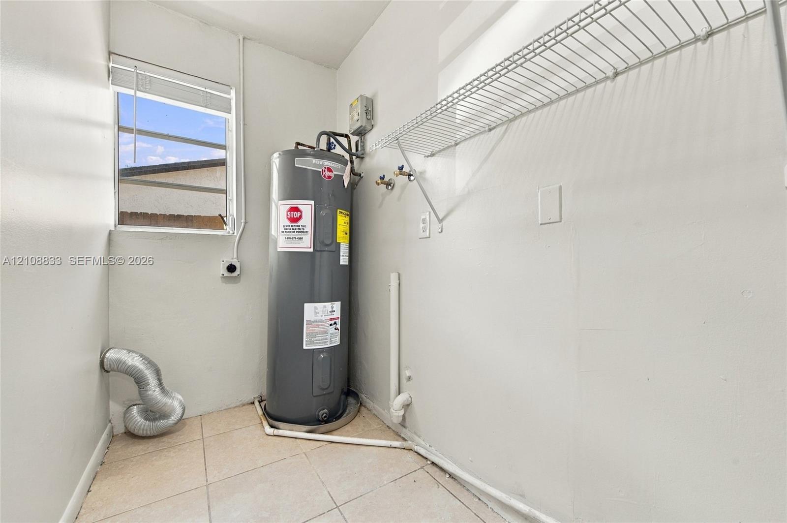 Utility area featuring tile flooring, a window, wall-mounted wire shelving, and a water heater